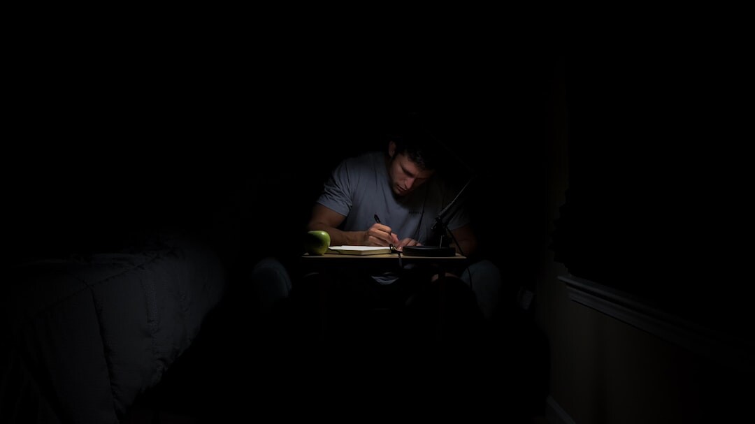 Croatian mystery writer sitting at a wooden desk writing in a notebook by lamplight